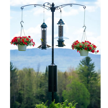 Brome Raccoon Buster® Guardian Pole System with bird feeder, surrounded by flowers, designed to deter raccoons and squirrels, ensuring uninterrupted bird feeding.